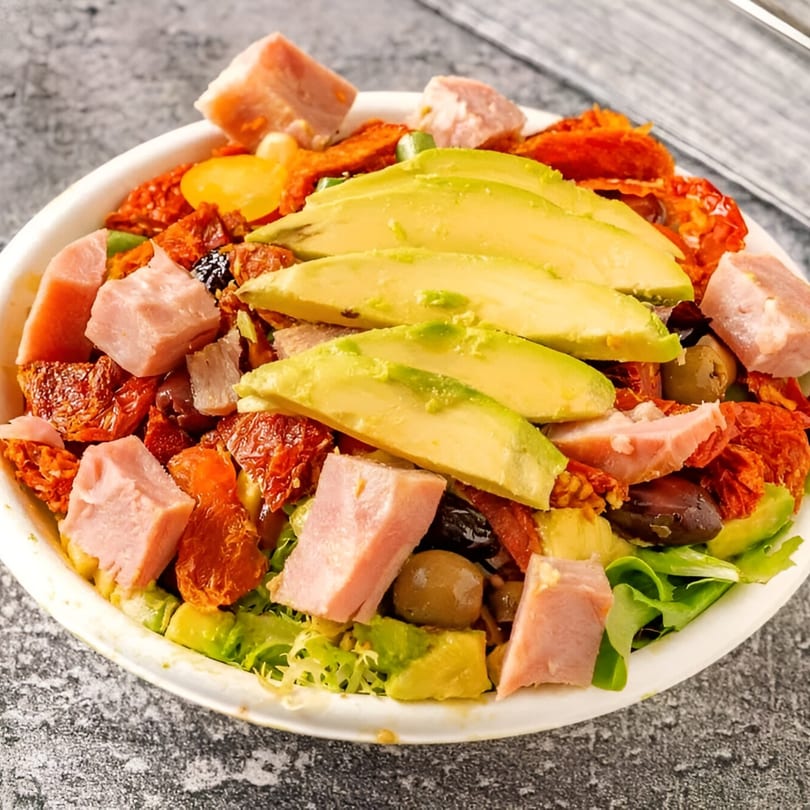 Delico 21 Gourmet Deli salad with avocado, ham, sun-dried tomatoes, and olives in a white bowl.
